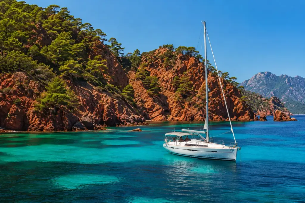 Segelyacht in einer tuerkisen Bucht mit roten Felsen auf Korsika